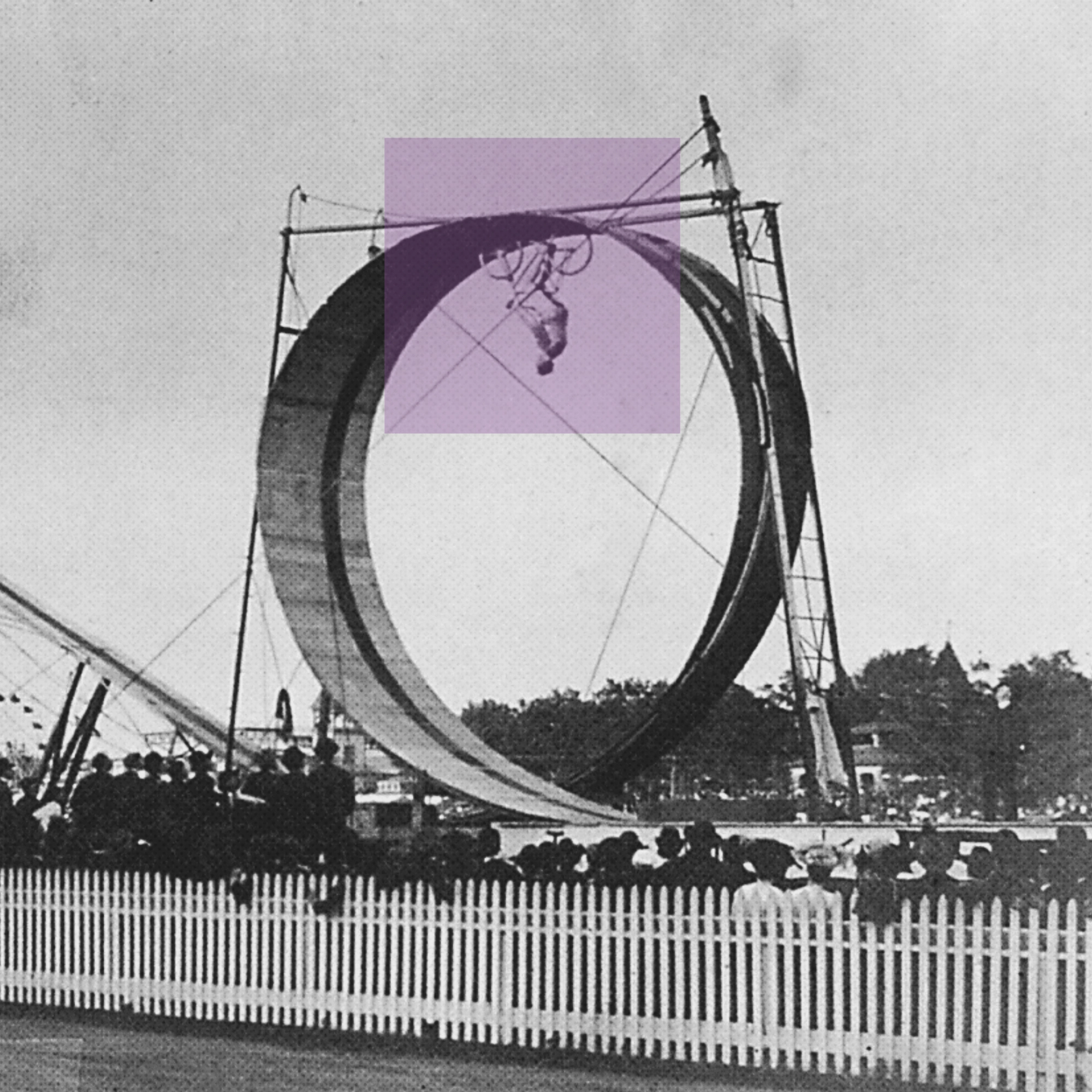 Black and white photo of a biker performing a stunt upside down inside a large circular ramp with a crowd watching.