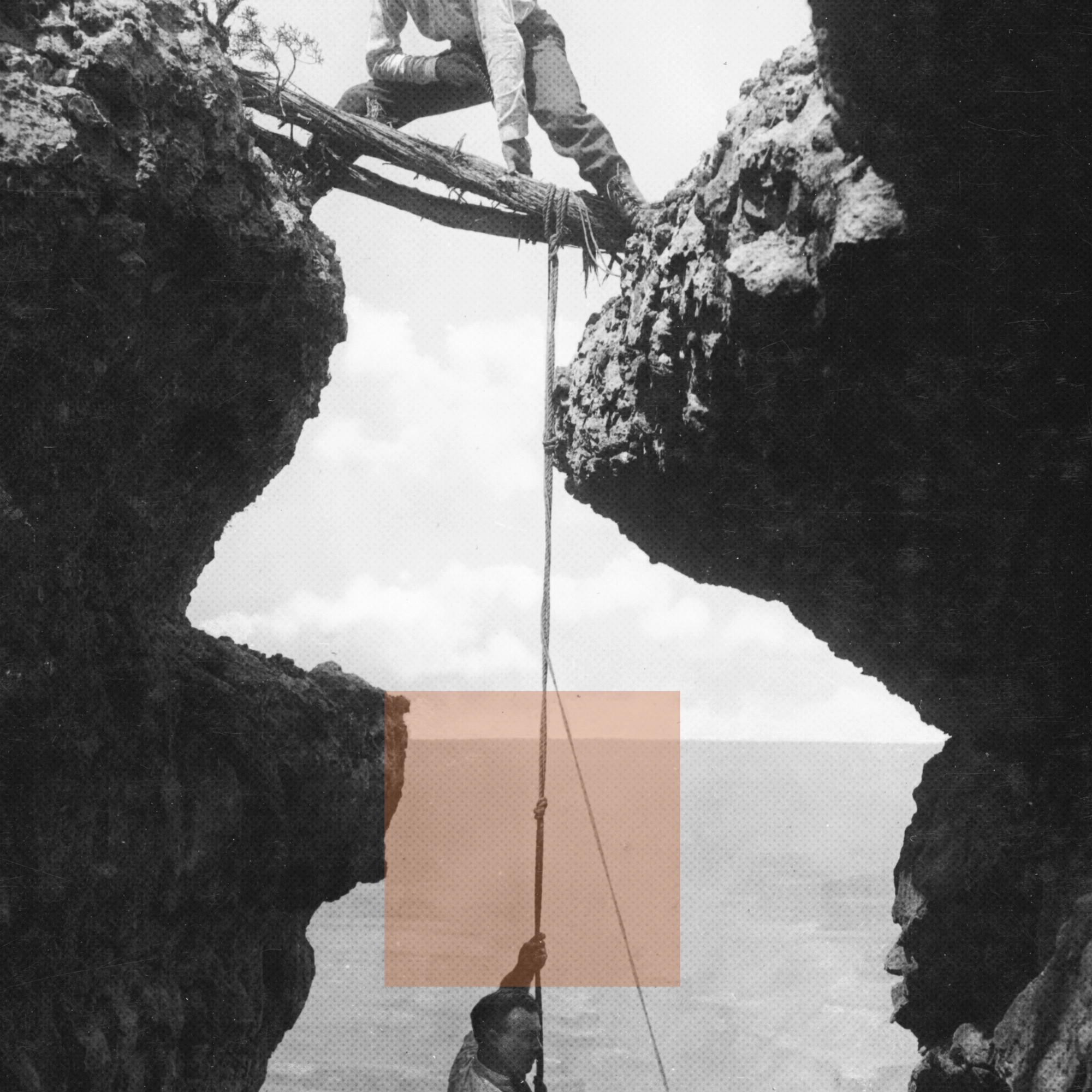 Man climbing up rocky cliffs using rope tied to logs bridging a gap between cliffs.