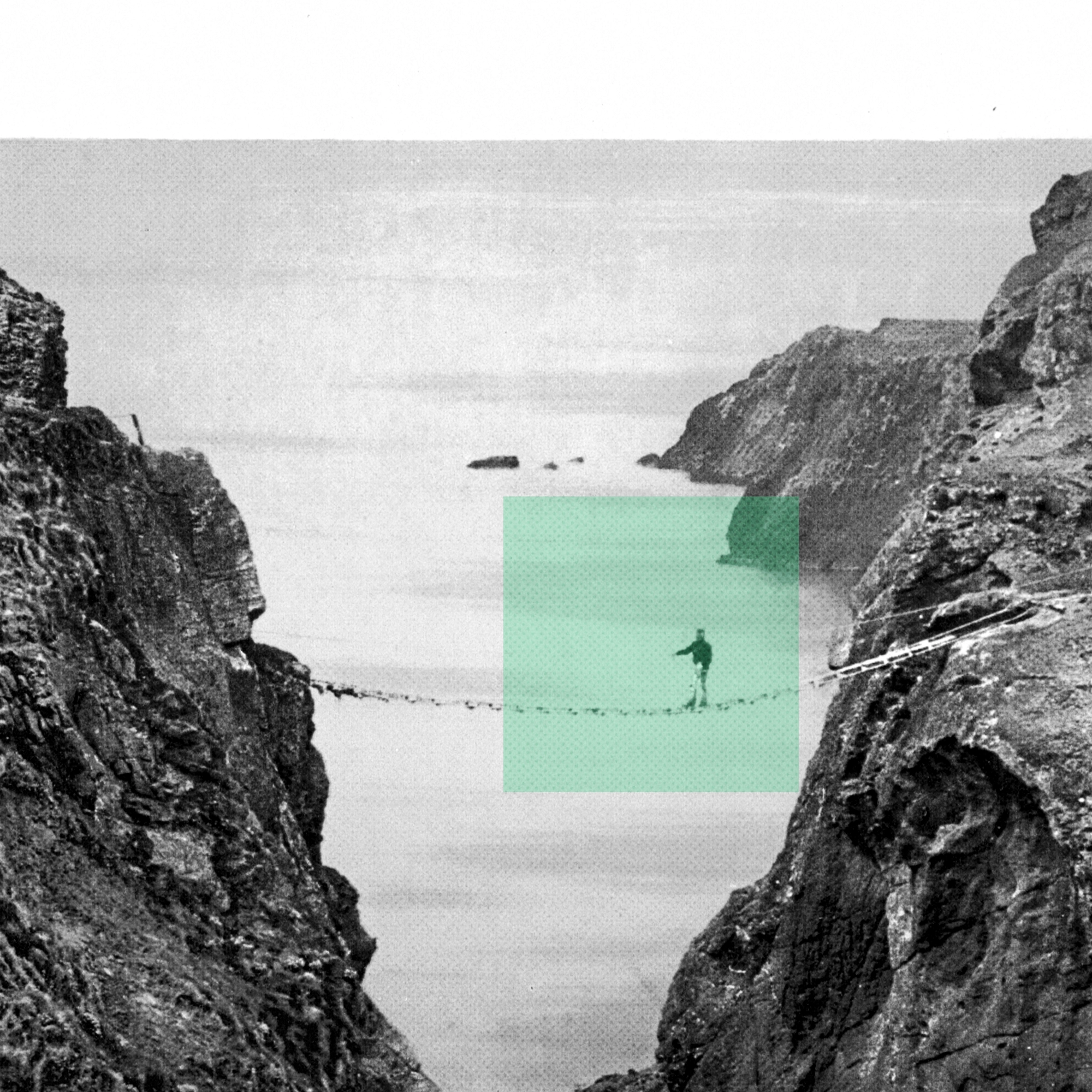 Person walking on a narrow rope bridge suspended between two rocky cliffs over the water.